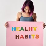 Asian woman holding a colorful 'Healthy Habits' sign in a studio setting, promoting wellness.