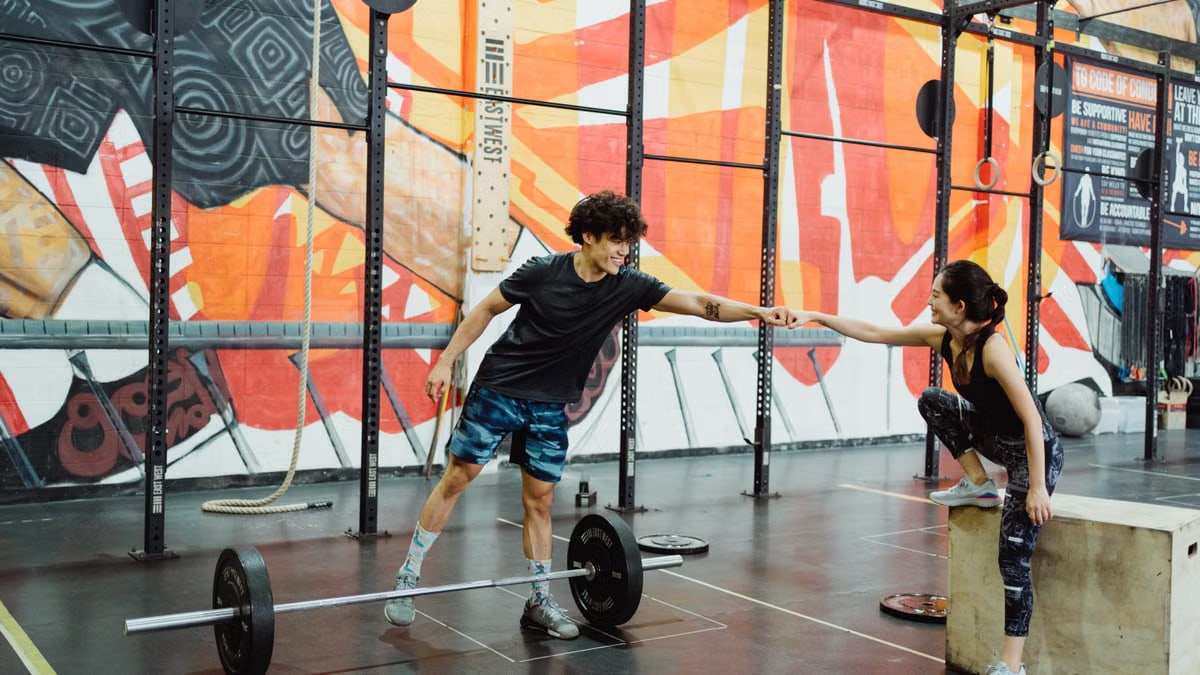 Cheerful gym interaction between a man and woman sharing a fist bump in a vibrant fitness environment.